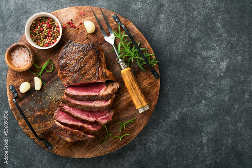 Steaks. Sliced grilled meat steak New York or Striploin with spices rosemary and pepper on black marble board on old stone grey background. Top view. Mock up.