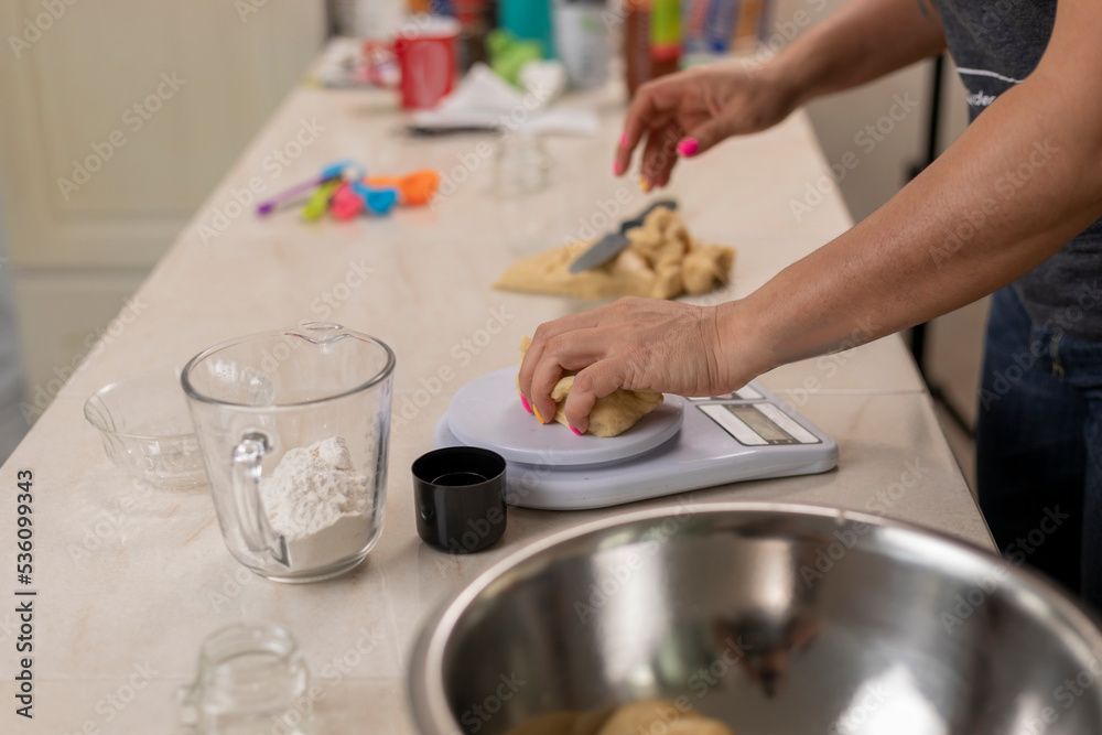 Woman's hands weighing portions of dough, to make pan de muerto at her kitchen counter