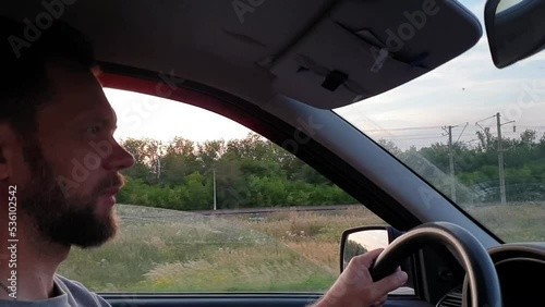 a bearded man driving a car on a summer evening on a country highway