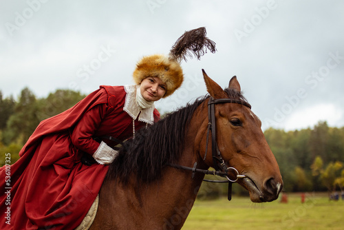 Portrait of a smiling woman in a red dress and 17th century hat on a horse, close-up