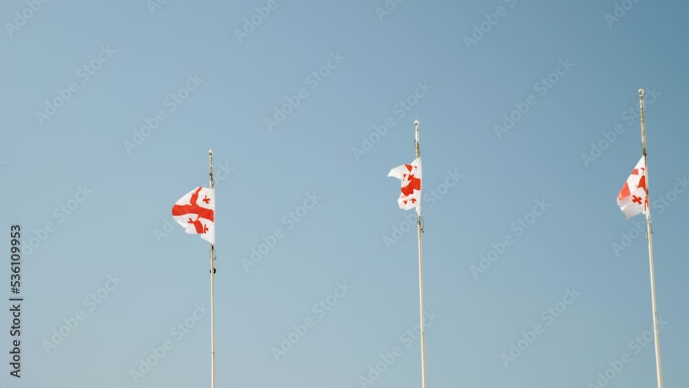 Three Georgian flags developing in the wind. In the background is a blue sky. Slow motion