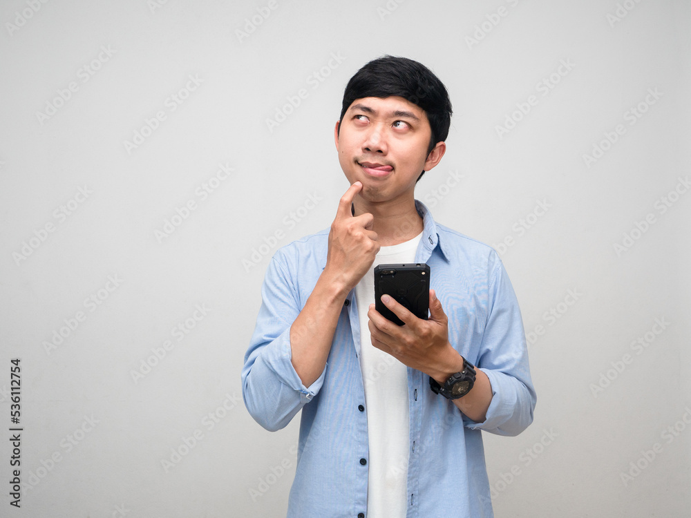Young man blue shirt hold mobile phone gesture hungry and thinking about food isolated Young man blue shirt hold mobile phone gesture hungry and thinking about food isolated