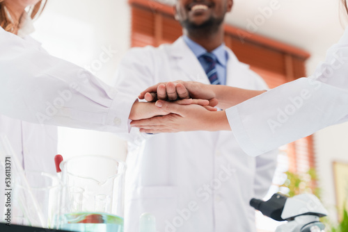 Scientists or researchers from a multi-ethnic team linking hands in a teamwork gesture.