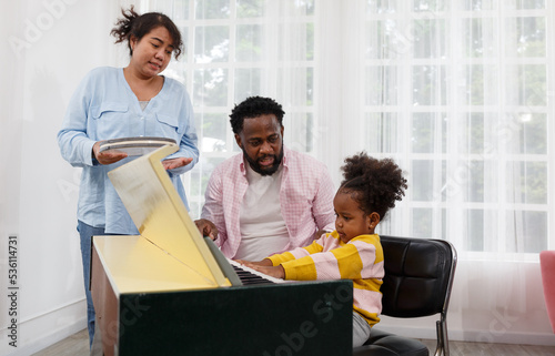 Parents are teaching their young daughter to play the piano or electone in the living room of the house. photo