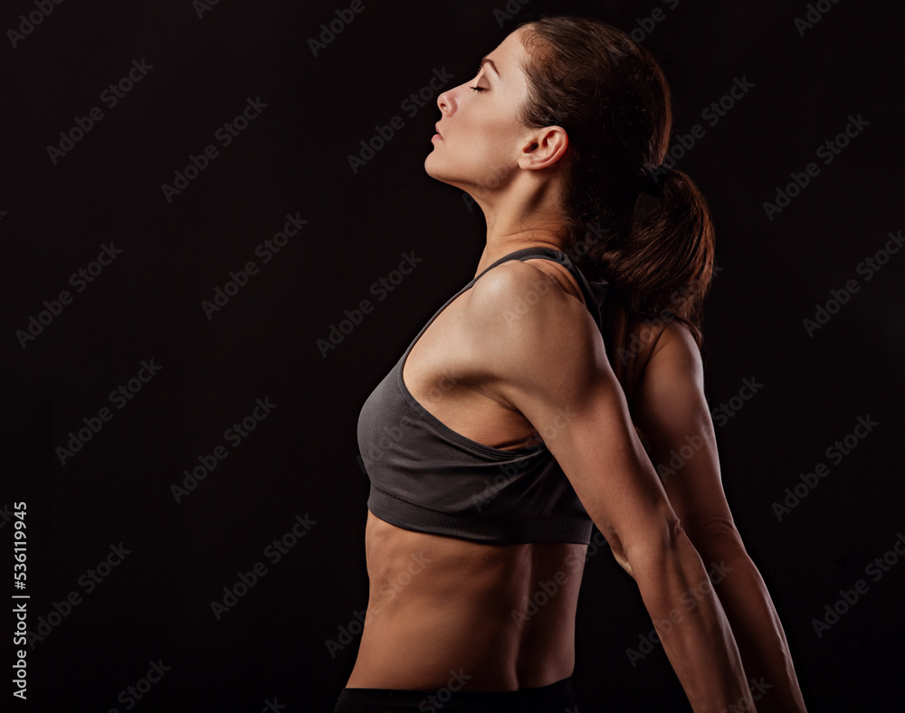 Strong sporty woman doing the arms and shoulders stretching exercise holding the hands in fist behind the back to relaxing in sport wear. Sports exercising. Closeup. Concept Strong sporty woman doing the arms and shoulders stretching exercise holding the hands in fist behind the back to relaxing in sport wear. Sports exercising. Closeup. Concept