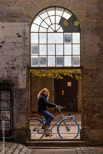 Photography Copenhagen, Denmark A woman cyclist maneuvers a bicycle over a astoop on Reffen island under an arched passageway