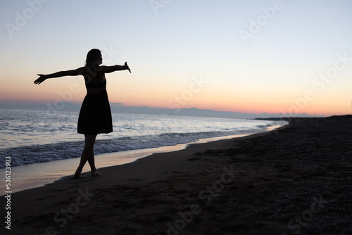 Woman standing with open arms on seashore at sunset