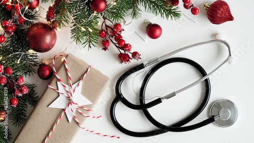 Christmas medical banner.Close up gift box,fir branches, cones,fir trees,red balls and stethoscope on white background,top view,flat lay,copy space.New Year's medicine,congratulations for the doctor.