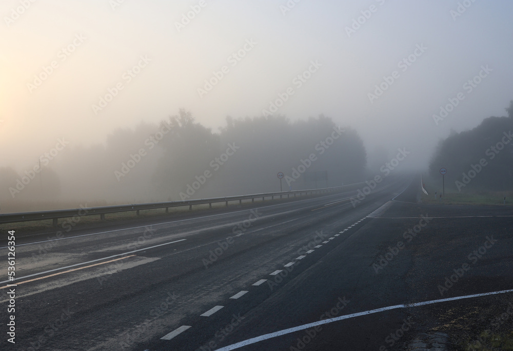 An asphalt road in the early morning in a dense fog. Selective focus.