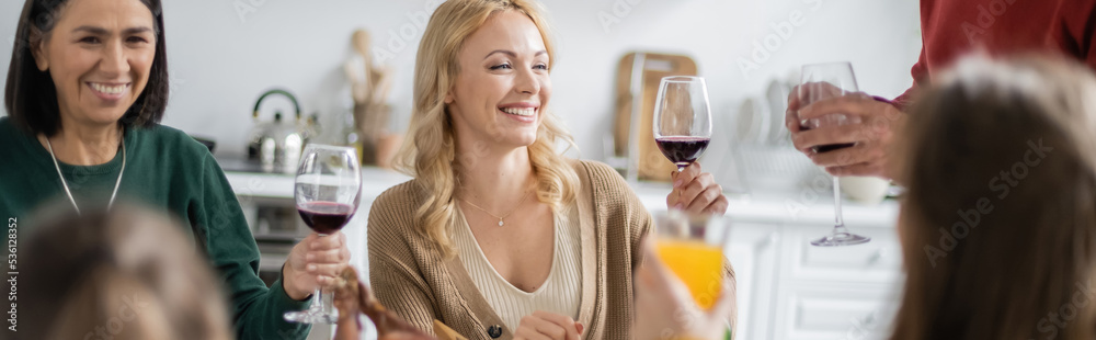 Smiling multiethnic family holding glasses of wine during thanksgiving celebration at home, banner Smiling multiethnic family holding glasses of wine during thanksgiving celebration at home, banner