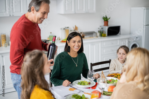 Multiethnic woman sitting near family and tasty thanksgiving dinner in kitchen