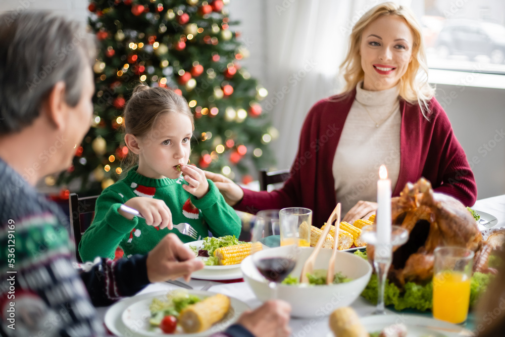 girl with fork having christmas dinner near blurred grandfather and smiling mom girl with fork having christmas dinner near blurred grandfather and smiling mom