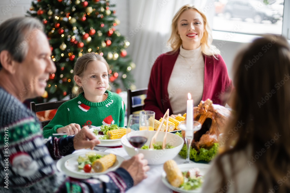 cheerful woman looking at family during festive dinner near christmas tree cheerful woman looking at family during festive dinner near christmas tree