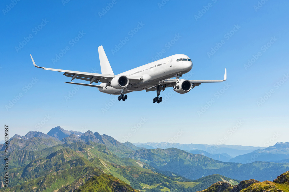 Obraz premium Airplane is flying over low clouds and mountains with autumn forest. Amazing landscape with passenger airplane, trees, mountains, blue cloudy sky. Passenger aircraft. Business commercial plane.