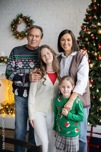 cheerful interracial grandparents with granddaughters looking at camera in decorated living room