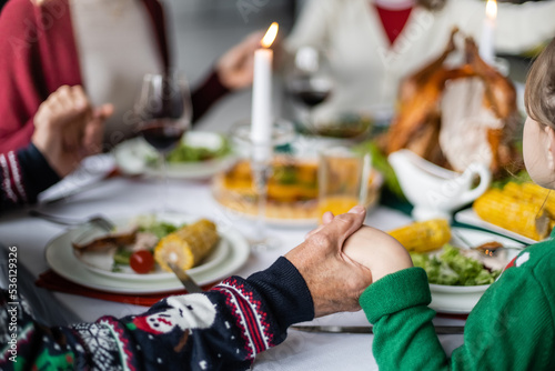 partial view of family holding hands during pray before thanksgiving dinner on blurred background