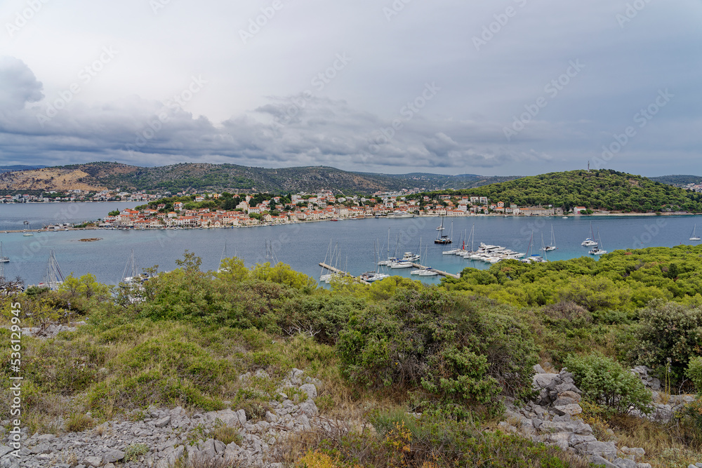 The village of Rogoznica on the Croatian Mediterranean coast photographed from a panoramic mountain. In the foreground green bushes, the blue sea with sailing ships.