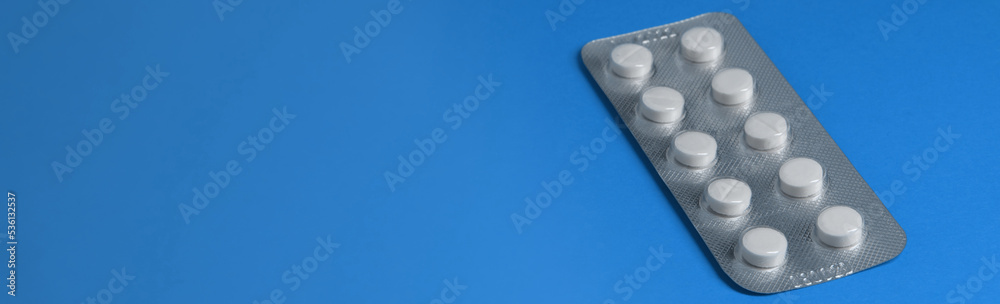 Package with white pills in a package on a blue background. Banner on medical theme, free space for text, copy space Package with white pills in a package on a blue background. Banner on medical theme, free space for text, copy space
