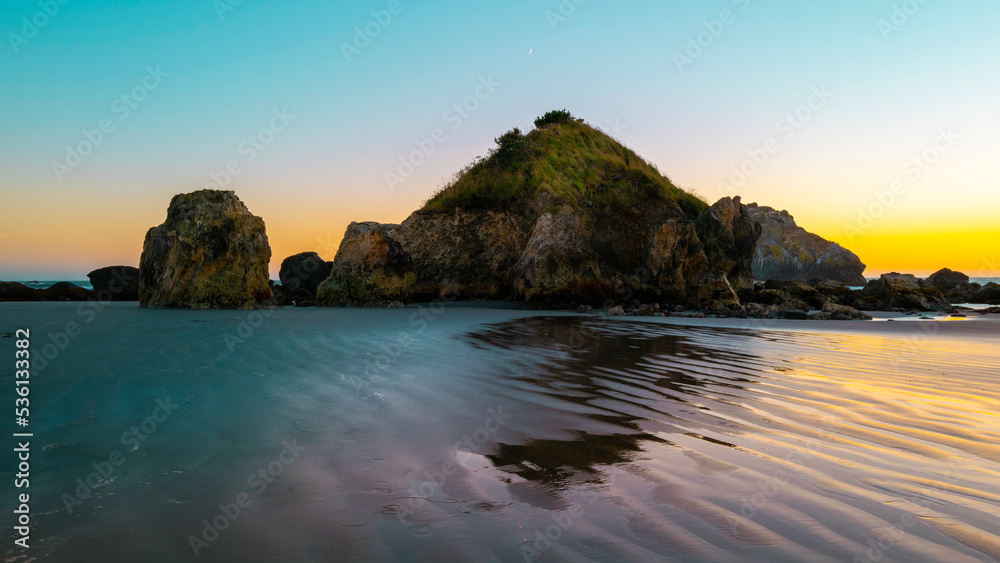 Seascape of rock islands and reflections on the wet beach sand, at sunrise during low tide on Pebble Beach in Crescent City, Northern California
