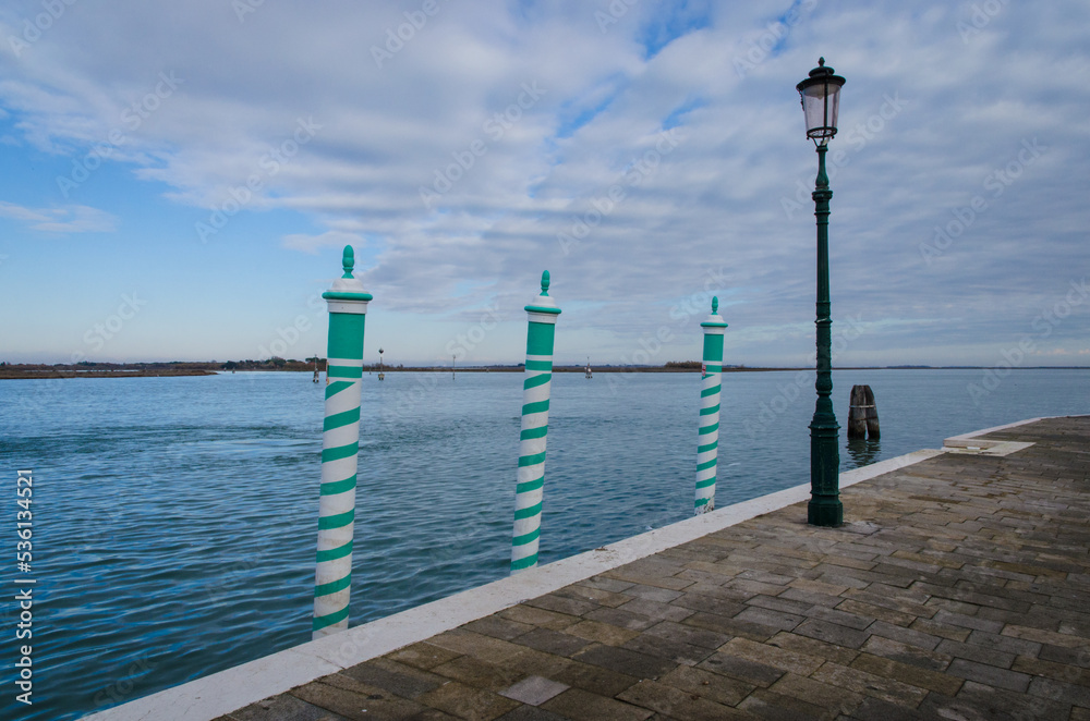 Tre paline bianche e verdi, i tipici pali da ormeggio veneziani, affacciati sulla laguna di Venezia in una giornata nuvolosa