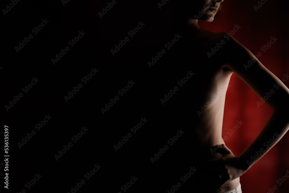Naked body silhouette of woman with her hands on her hips on darkness red background with copyspace.