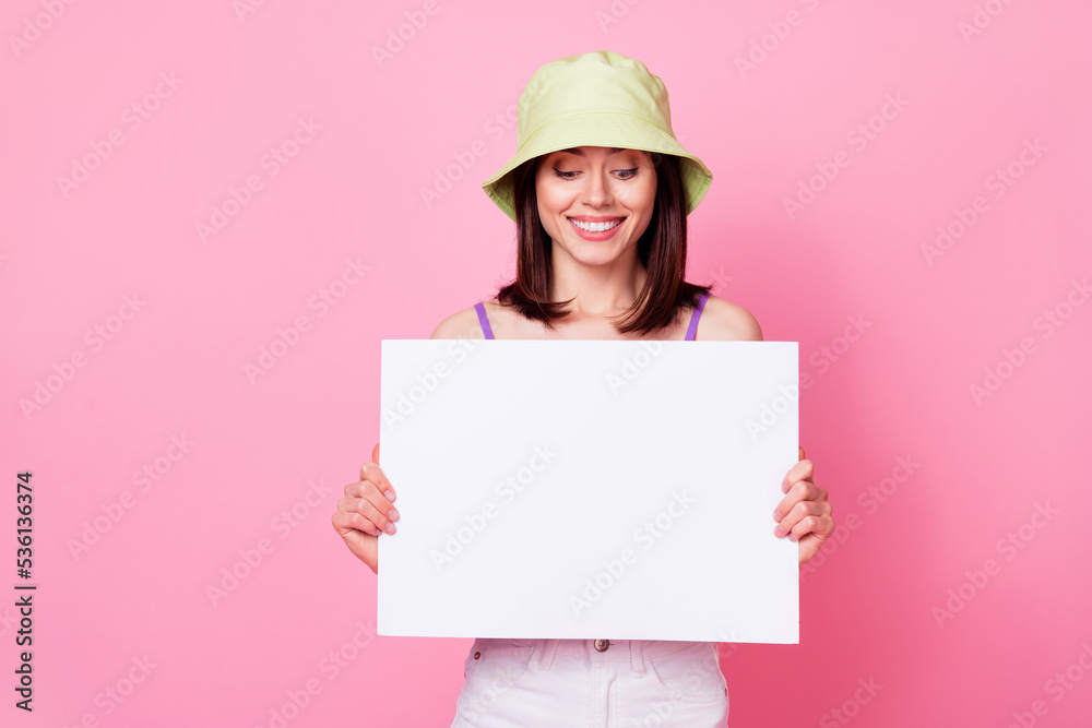 Photo of attractive young woman hold look empty paper card ad promotion wear stylish tank top headwear isolated on pink color background Photo of attractive young woman hold look empty paper card ad promotion wear stylish tank top headwear isolated on pink color background