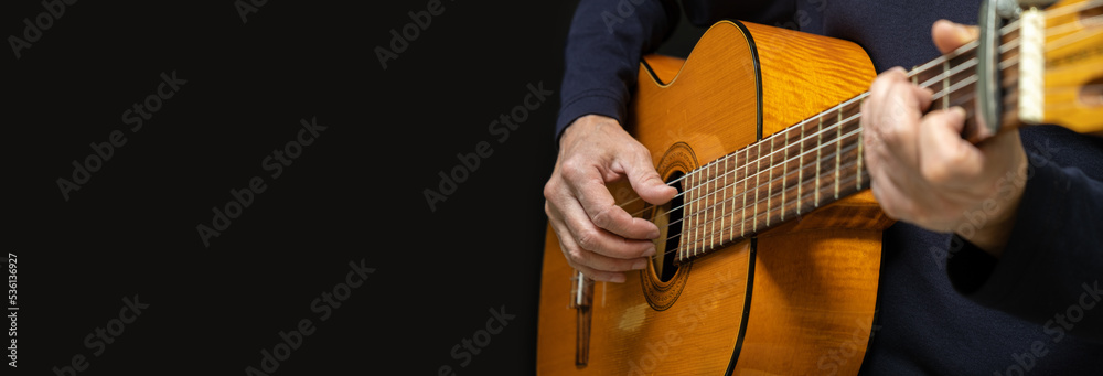 Obraz premium Guitarist playing acoustic guitar on black background, selective focus. A male musician plays the guitar. cover for online courses learning at home. A man playing guitar. Long wide banner, copy space