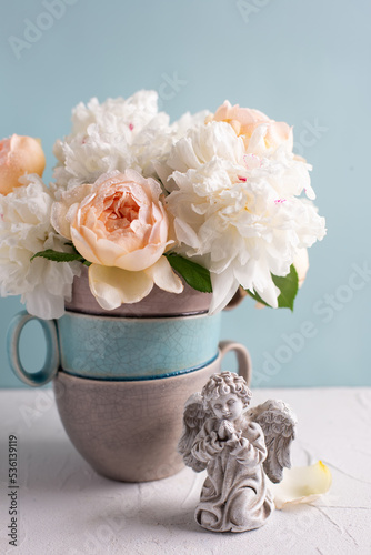 Postcard with angel and romantic summer roses and peonies flowers  against blue  wall in vase. Selective focus. Still life.  Place for text. Romantc concept..
