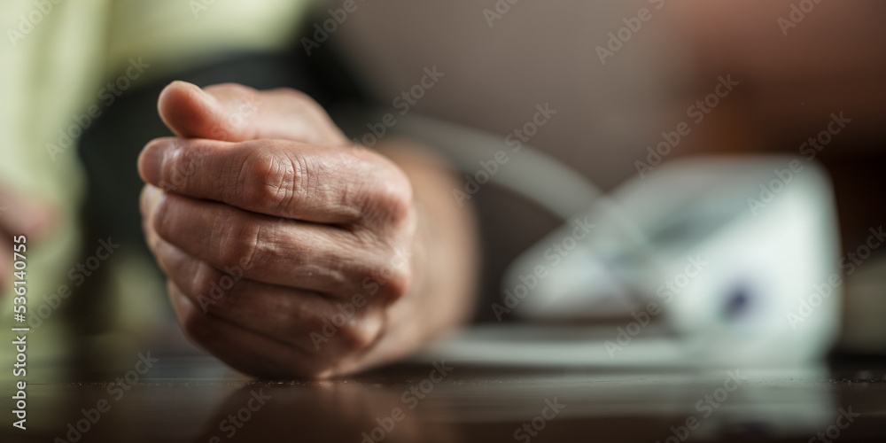 Fototapeta premium Older man measures his blood pressure with digital medical instrument. Hand of person lies on table during medical examination.
