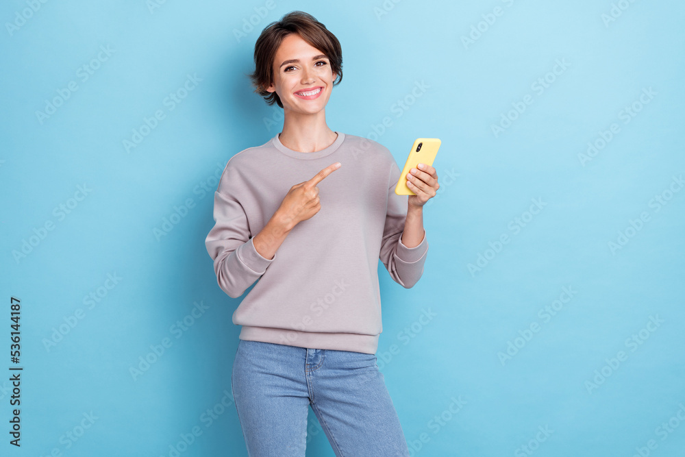 Portrait of sweet positive girl bob hairstyle wear gray sweatshirt directing on phone recommend app isolated on blue color background