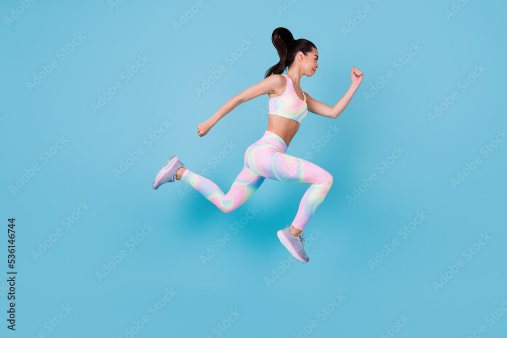 Full length photo of purposeful strong woman dressed sport costume jumping up running fast isolated blue color background Full length photo of purposeful strong woman dressed sport costume jumping up running fast isolated blue color background