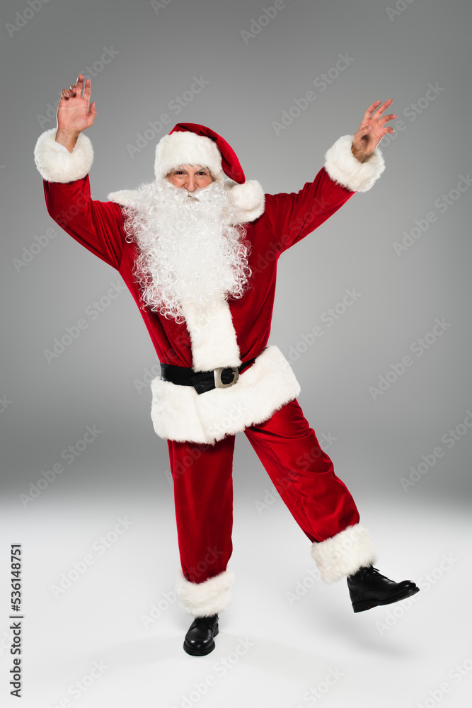 Full length of santa claus in costume dancing on grey background.