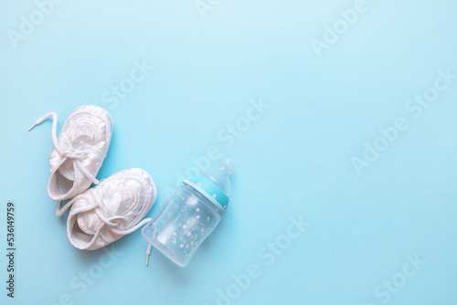 baby booties and bottle for milk formula on a blue background with copy space