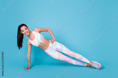 Full length photo of cute cheerful young woman dressed sport costume standing one hand arm plank isolated blue color background