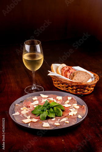 romantic dinner with carpaccio cold meats basket of artisan breads basil leaves dijon mustard glass of white wine wooden table