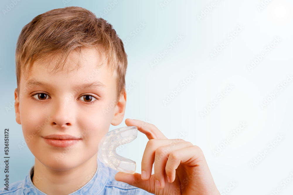 Positive child boy is holding mouth guards for his teeth and smiling