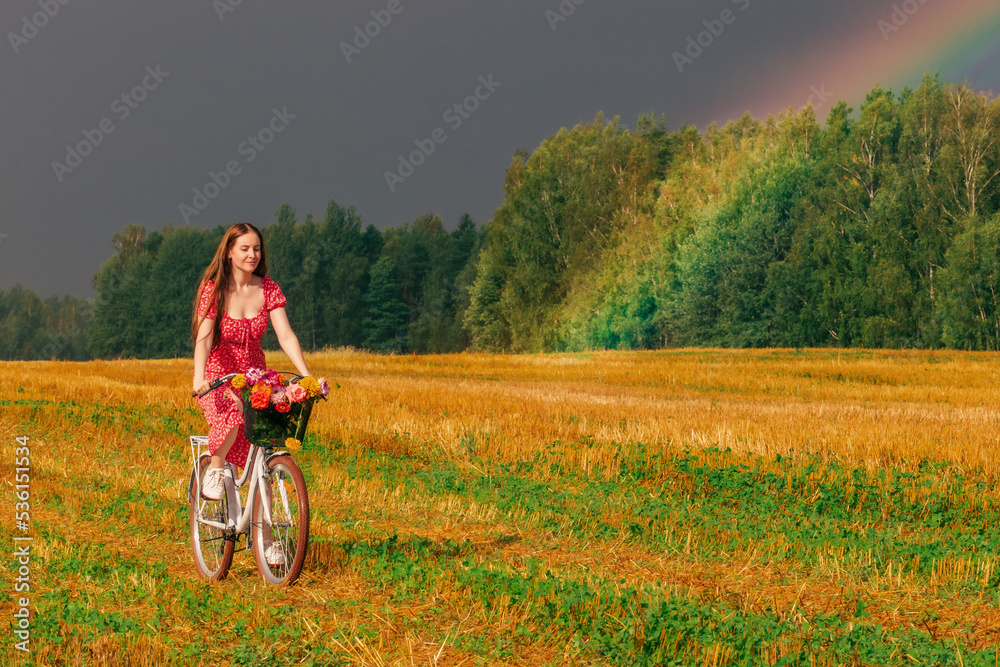 Young pretty woman rides a bike across the field past the rainbow Young pretty woman rides a bike across the field past the rainbow