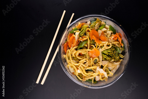 Chinese food delivery vegetarian yakisoba bowl top view black background with chopsticks