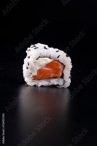 japanese oriental food was just a piece of raw salmon sushi with cream cheese and sesame isolated on black background viewed from the front