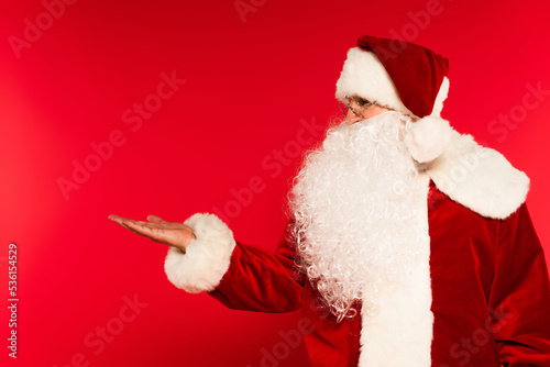 Bearded santa claus pointing with hand on red background.