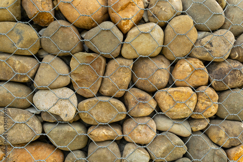 Texture, stone wall background. Stones on the background of a fence made of metal mesh.