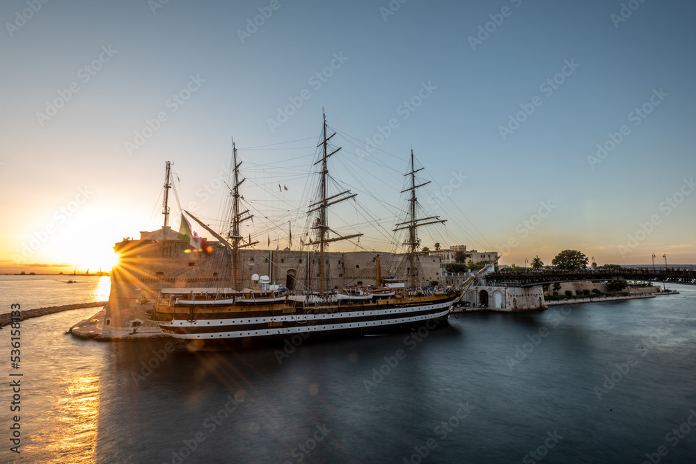 Fototapeta premium The Italian Navy Historical Ship Called Amerigo Vespucci Moored in front of the Aragonian Castle in the Canalboat of Taranto at Sunset, in the South of Italy