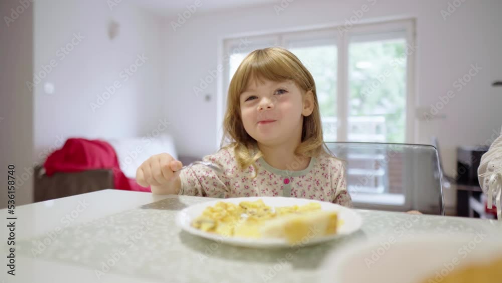 Child has a good appetite. Baby eats breakfast by herself, enjoying the food. Healthy meal. Forming the right habits from a young age. Little girl chews, smiles and points to something with her finger Child has a good appetite. Baby eats breakfast by herself, enjoying the food. Healthy meal. Forming the right habits from a young age. Little girl chews, smiles and points to something with her finger