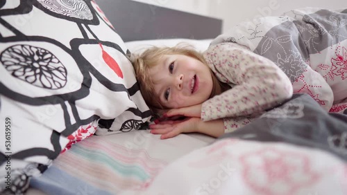 The child wakes up in the morning in a good mood. The mometn the kid wakes up after a day sleep. Baby luxuriates in the bed in the parent's bedroom. Bed linen with different patterns.