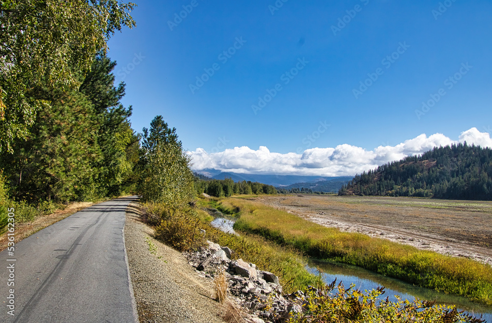 On a sunny Autumn day in Northwestern Idaho, The Trail of the Coeur d'Alenes passes between forested hillsides and a small stream in a mountain valley.