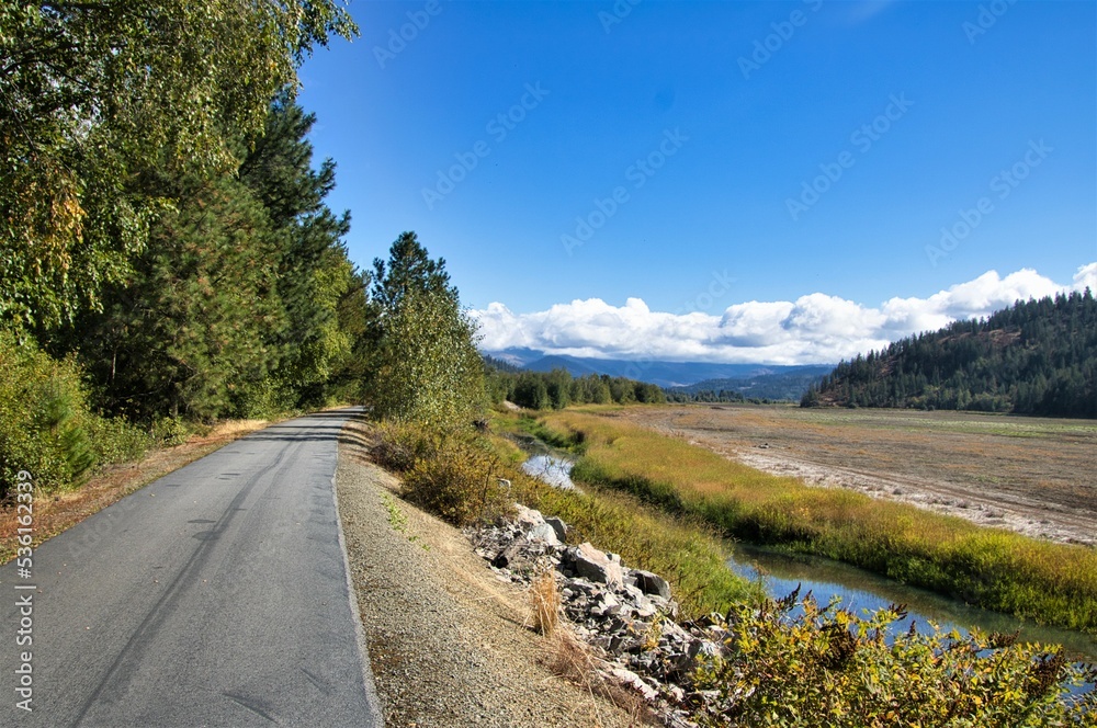 On a sunny Autumn day in Northwestern Idaho, The Trail of the Coeur d'Alenes passes through a mountain valley between a small stream and a forested hillside.