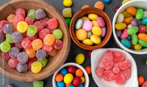 Assorted colorful candies in bowls over stone background