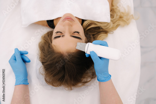 First-person view of cosmetologist doing beauty procedure at cosmetology clinic. Beautician using peeling device, ultrasonic clining. Gorgeous woman