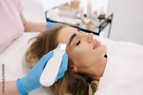 Young woman taking beauty procedure in spa salon. Beautician using peeling device, ultrasonic clining. Gorgeous woman