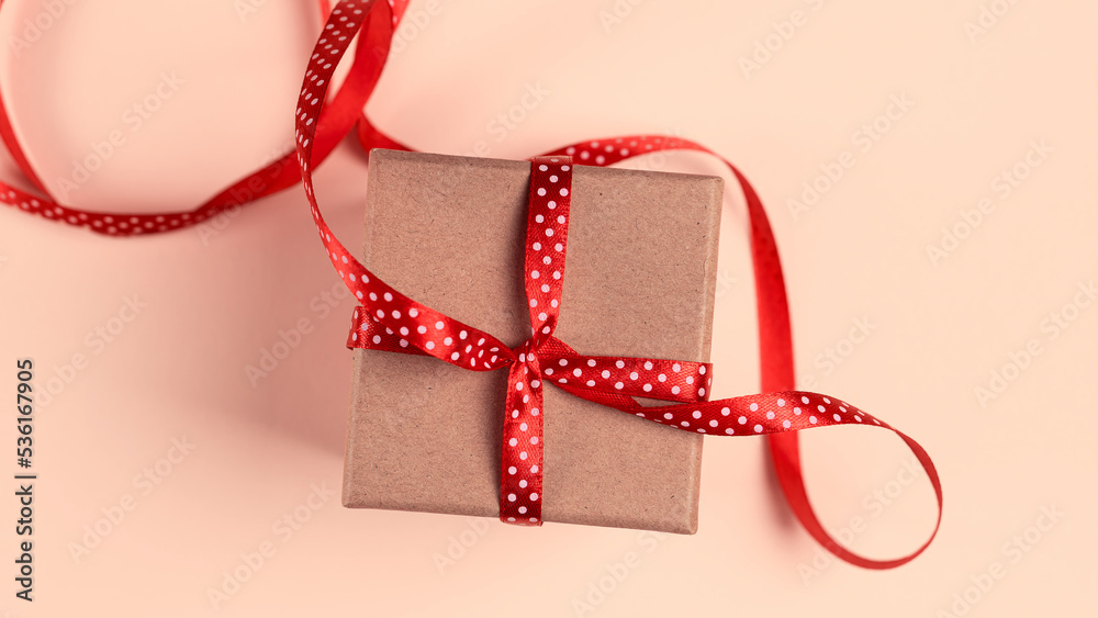 Gift box with red ribbon over pink paper background